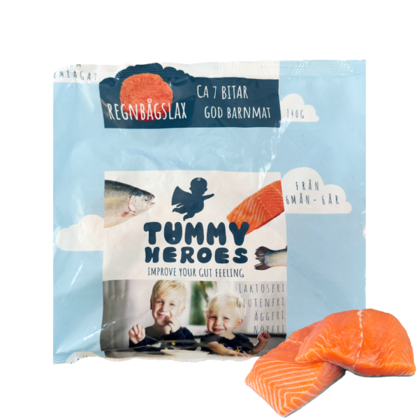 Förpackning av Tummy Heroes barnmat med regnbågslax, med blå bakgrund och en siluett av en bebis samt texten 'Tummy Heroes'. På förpackningen syns en bild av två glada barn, regnbågslaxfiléer och symboler som visar att produkten är laktosfri, glutenfri, äggfri och nötfri. Svensk flagga och en färsk bit regnbågslax är placerad bredvid förpackningen.